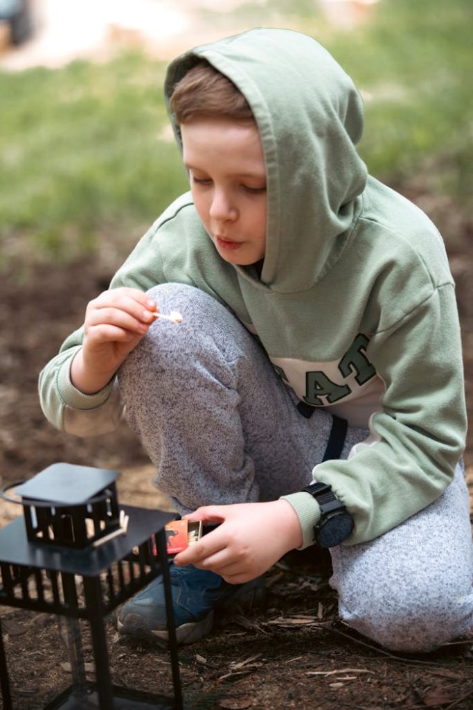 Young boy lighting a lantern outdoors in a forest. Peaceful and serene setting.