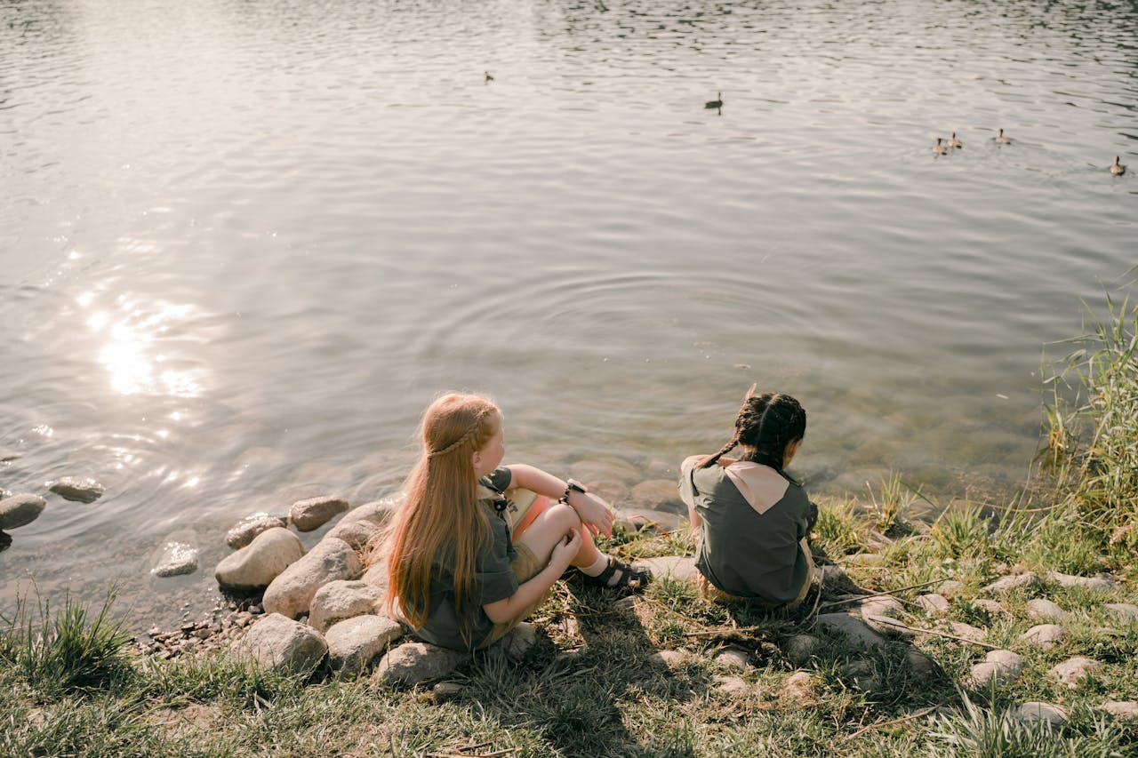 Two children enjoy a peaceful moment by the lake, surrounded by nature and tranquility.